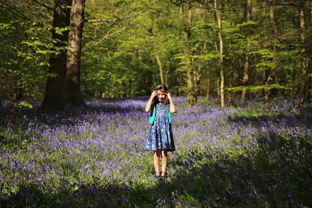 Eastbourne_family_photographer_bluebells_powell-ful_photography.1 your girl standing in the middle of a woodland with bluebells all over the ground. pulling her hair out of her eyes