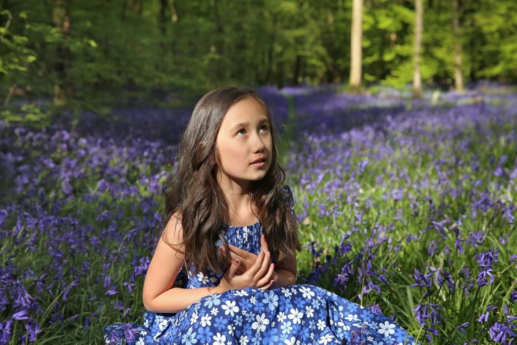 Eastbourne_family_photographer_bluebells_powell-ful_photography young girl sittling in a woodland surrounded by bluebells, girl is looking up