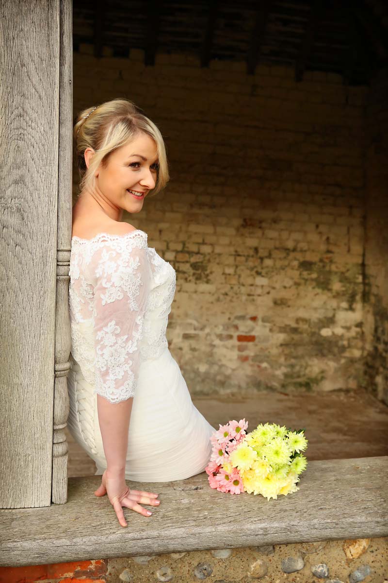 bride sitting on a ledge, leaning against a wall. bouquet on the ledge