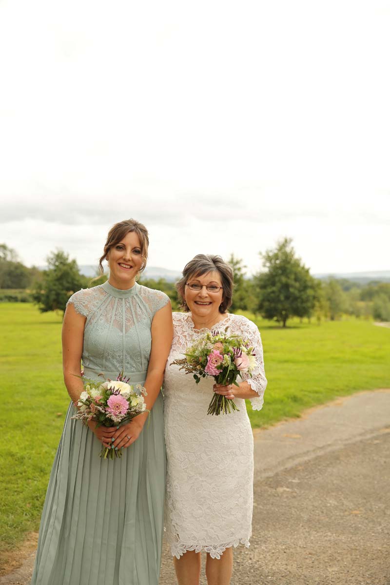 bride standing next to bridesmaid both tolding there bouquets