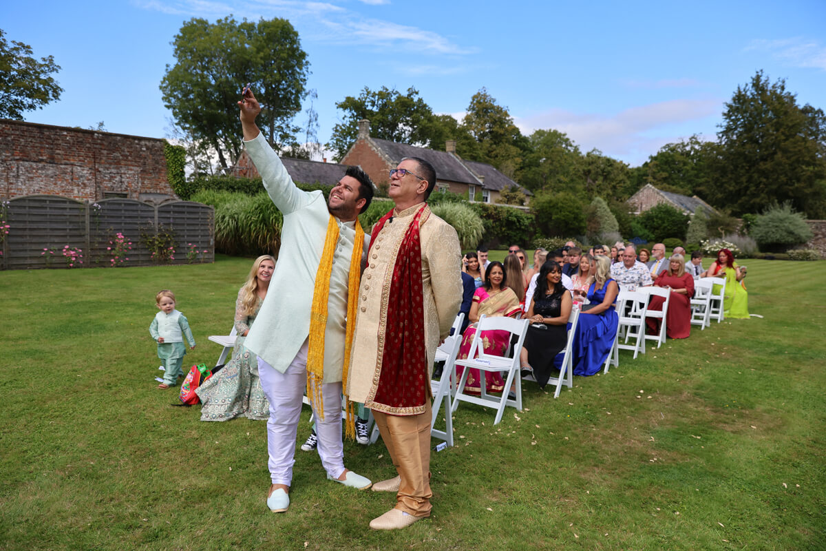 Indian wedding ceremony outside at Wadhurst Castle, groom taking a picture on his phone