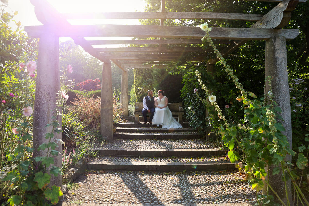 bride and groom sitting down on a bench, in a flower garden